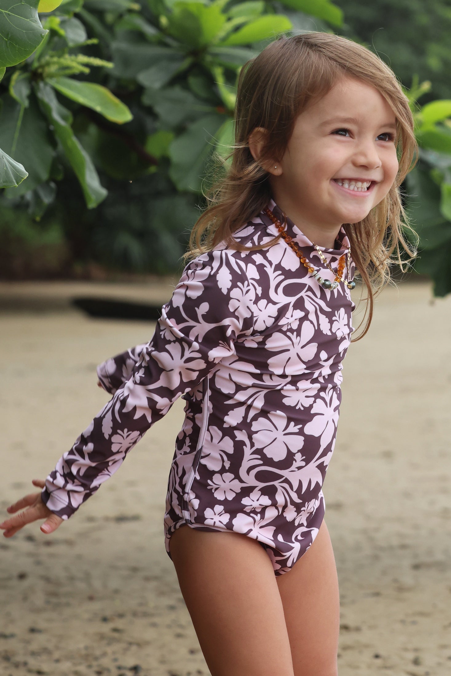 little girl wearing long sleeve one piece bikini in blush and brown hibiscus print.