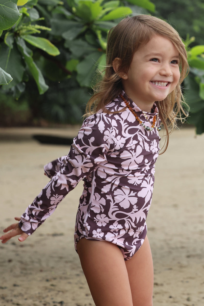 little girl wearing long sleeve one piece bikini in blush and brown hibiscus print.