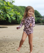 little girl wearing long sleeve one piece bikini in blush and brown hibiscus print.