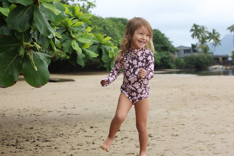 little girl wearing long sleeve one piece bikini in blush and brown hibiscus print.