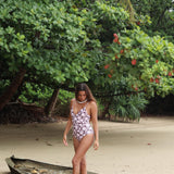 Woman with brown hair wearing a one piece v-neck bikini in blush and brown hibiscus print.