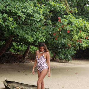 Woman with brown hair wearing a one piece v-neck bikini in blush and brown hibiscus print.