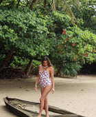 Woman with brown hair wearing a one piece v-neck bikini in blush and brown hibiscus print.
