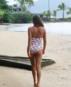 Woman with brown hair wearing a one piece v-neck bikini in blush and brown hibiscus print.