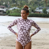 Woman with brown hair wearing a high neck long sleeve one piece bikini in blush and brown hibiscus print.