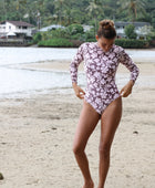Woman with brown hair wearing a high neck long sleeve one piece bikini in blush and brown hibiscus print.