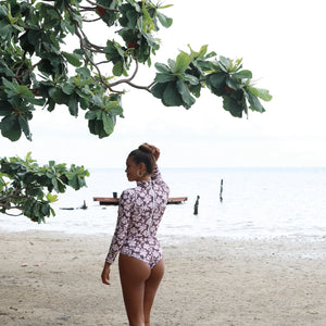 Woman with brown hair wearing a high neck long sleeve one piece bikini in blush and brown hibiscus print.