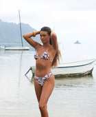 Woman with brown hair wearing a triangle bikini top and cheeky bikini bottoms in blush and brown hibiscus print.
