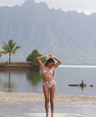 Woman with brown hair wearing a bikini top with a knot detail and a high waisted bikini bottoms in blush and brown hibiscus print.