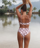 Woman with brown hair wearing a bikini top with a knot detail and a high waisted bikini bottoms in blush and brown hibiscus print.
