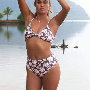 Woman with brown hair wearing a bikini top with a knot detail and a high waisted bikini bottoms in blush and brown hibiscus print.
