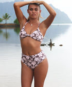 Woman with brown hair wearing a bikini top with a knot detail and a high waisted bikini bottoms in blush and brown hibiscus print.