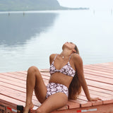 Woman with brown hair wearing a bikini top with a knot detail and a high waisted bikini bottoms in blush and brown hibiscus print.