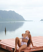 Woman with brown hair wearing a bikini top with a knot detail and a high waisted bikini bottoms in blush and brown hibiscus print.
