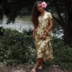 woman with brown hair wearing a maxi dress in a green color with naupaka pattern throughout. 