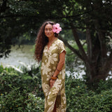 woman with brown hair wearing a maxi dress in a green color with naupaka pattern throughout. 