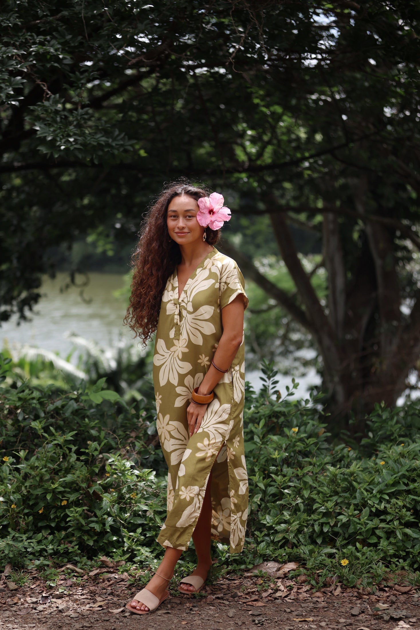 woman with brown hair wearing a maxi dress in a green color with naupaka pattern throughout. 