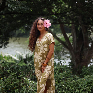 woman with brown hair wearing a maxi dress in a green color with naupaka pattern throughout. 