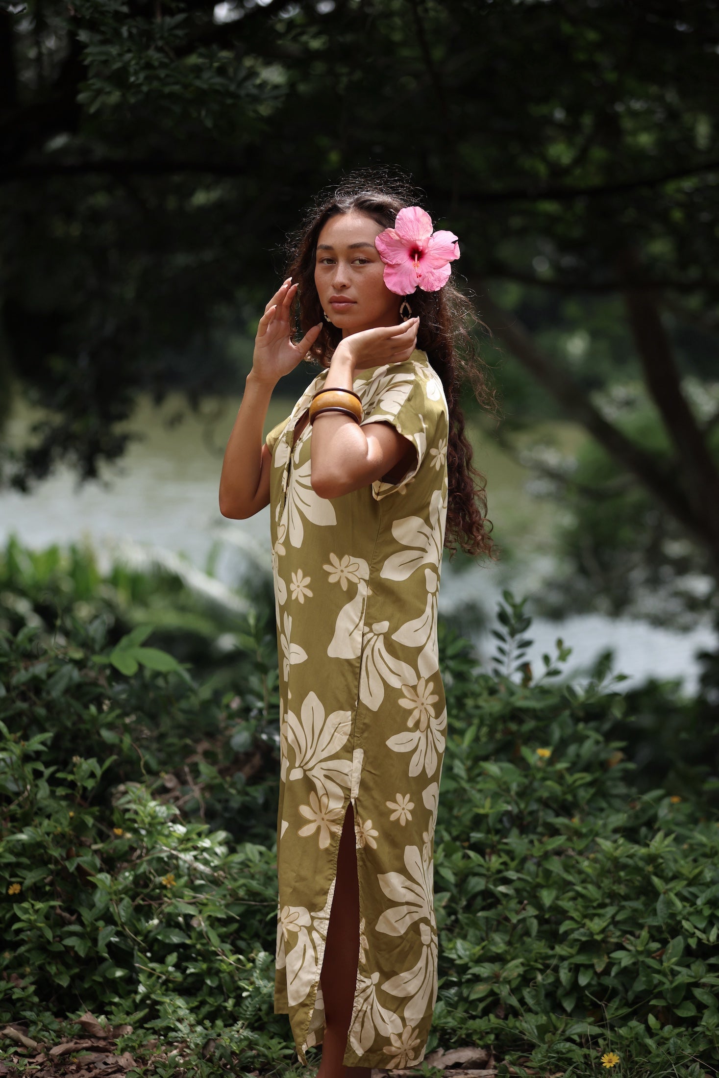 woman with brown hair wearing a maxi dress in a green color with naupaka pattern throughout. 