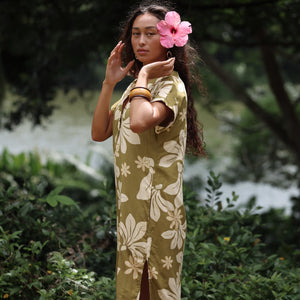 woman with brown hair wearing a maxi dress in a green color with naupaka pattern throughout. 