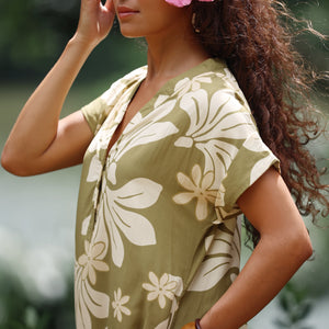 woman with brown hair wearing a maxi dress in a green color with naupaka pattern throughout. 