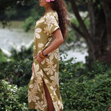 woman with brown hair wearing a maxi dress in a green color with naupaka pattern throughout. 