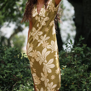 woman with brown hair wearing a maxi dress in a green color with naupaka pattern throughout. 