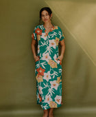 Woman wearing long short sleeve shirt dress with large multi colored floral print on green ground.