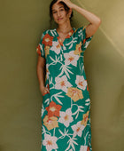 Woman wearing long short sleeve shirt dress with large multi colored floral print on green ground.