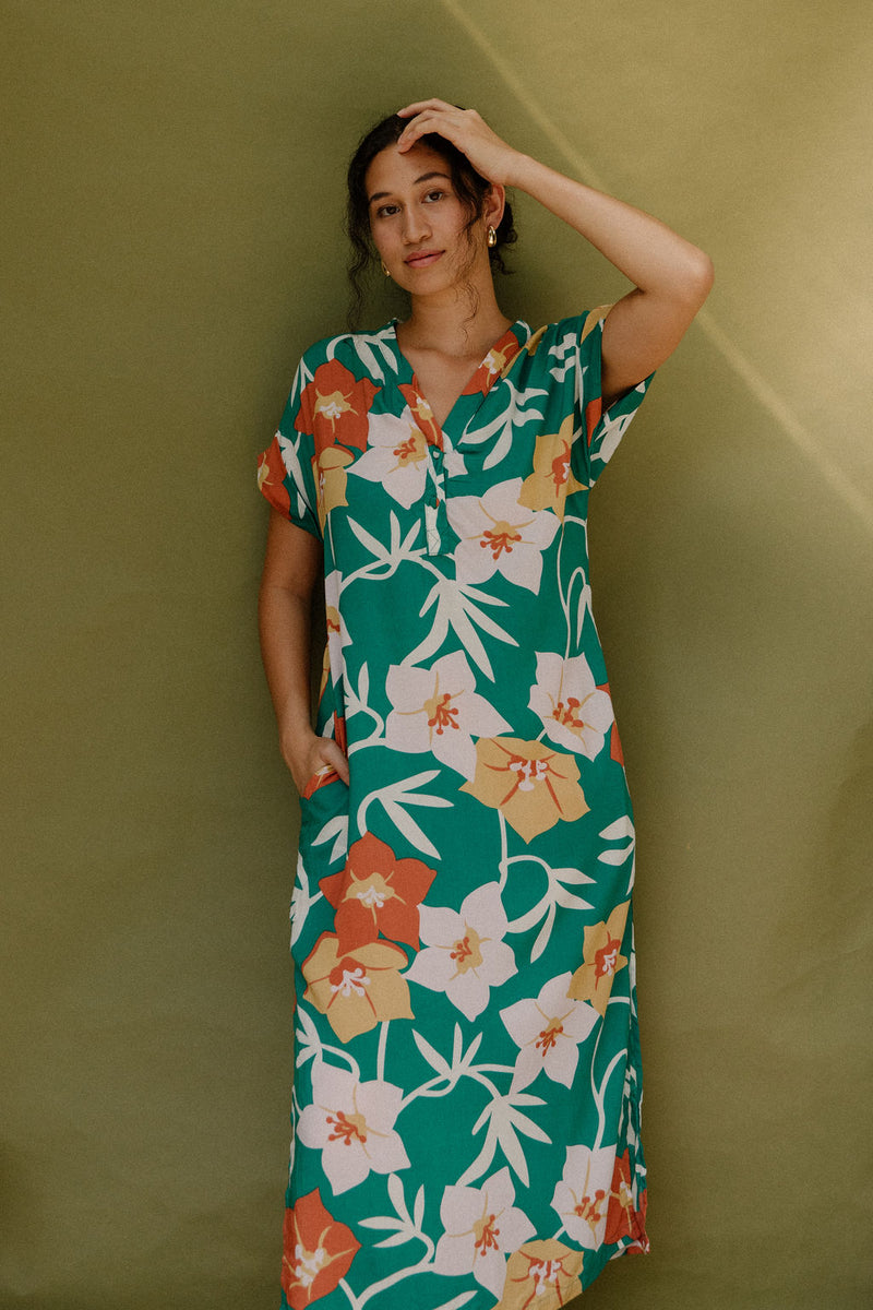 Woman wearing long short sleeve shirt dress with large multi colored floral print on green ground.