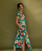 Woman wearing long short sleeve shirt dress with large multi colored floral print on green ground.