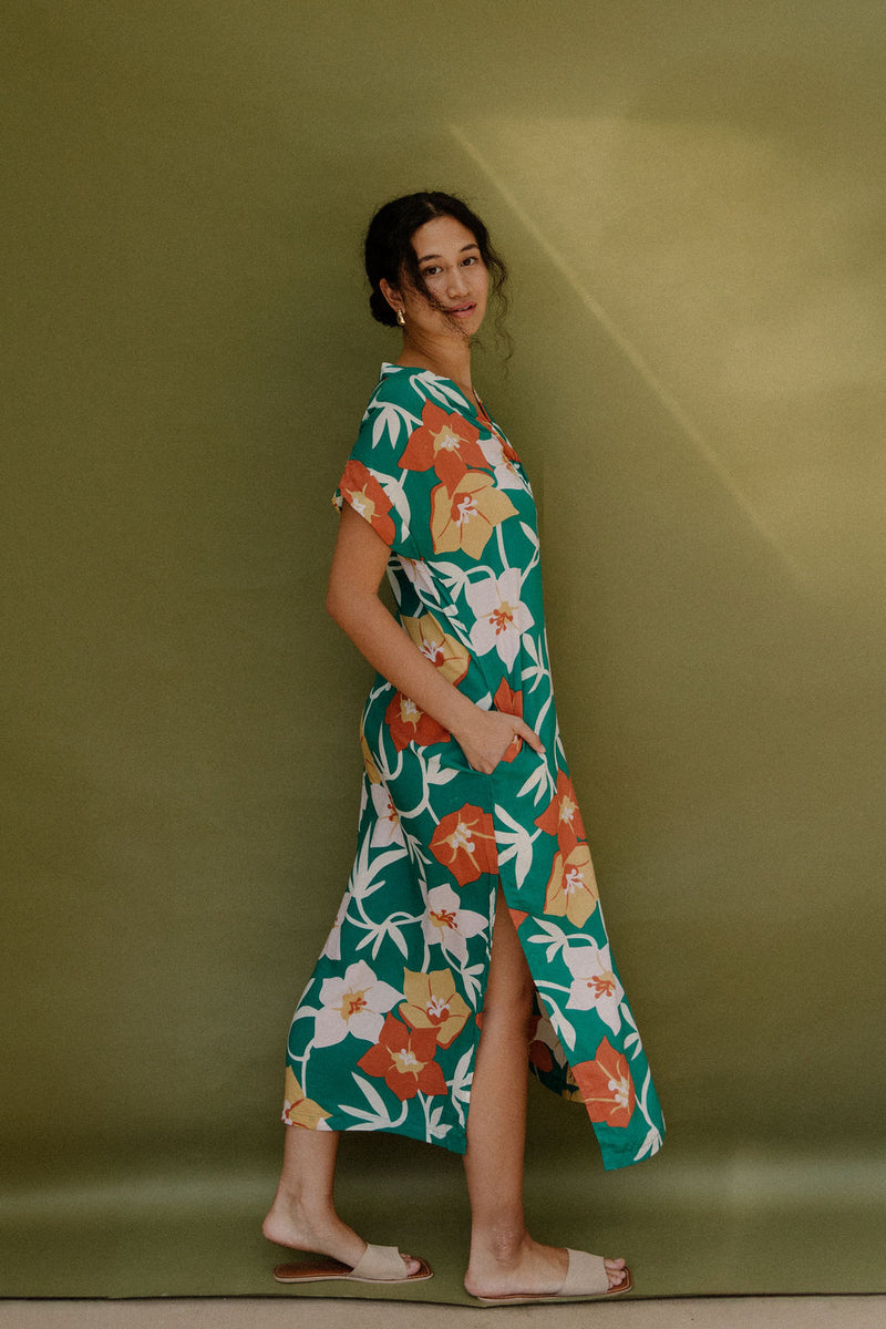 Woman wearing long short sleeve shirt dress with large multi colored floral print on green ground.