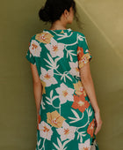 Woman wearing long short sleeve shirt dress with large multi colored floral print on green ground.