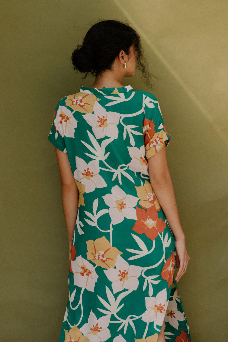 Woman wearing long short sleeve shirt dress with large multi colored floral print on green ground.