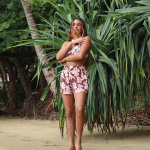 Woman with brown hair wearing a bikini top with a knot detail and flowy shorts in blush and brown hibiscus print.