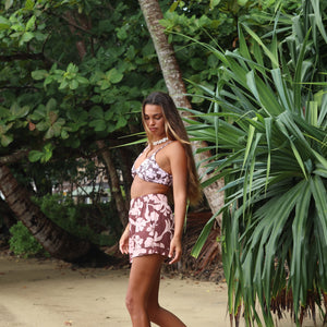 Woman with brown hair wearing a bikini top with a knot detail and a high waisted bikini bottoms in blush and brown hibiscus print.