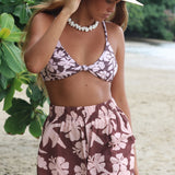 Woman with brown hair wearing a bikini top with a knot detail and flowy shorts in blush and brown hibiscus print.
