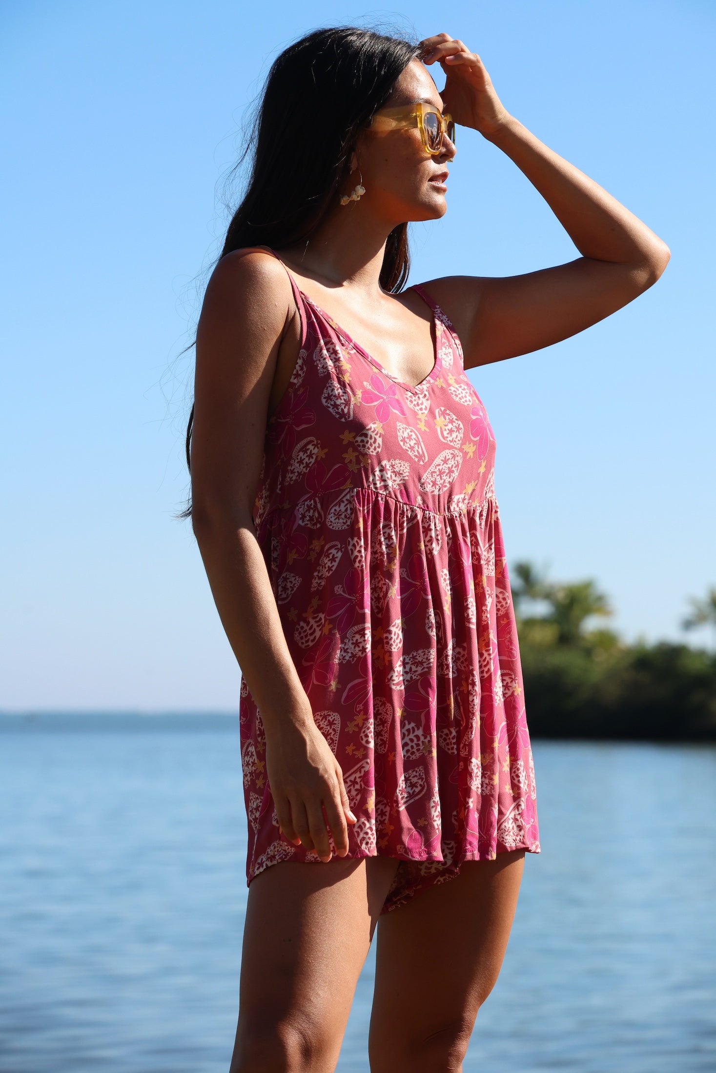 woman with brown hair wearing saghetti strap romper with shell and pua print in a pink color