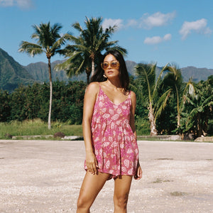 woman with brown hair wearing saghetti strap romper with shell and pua print in a pink color