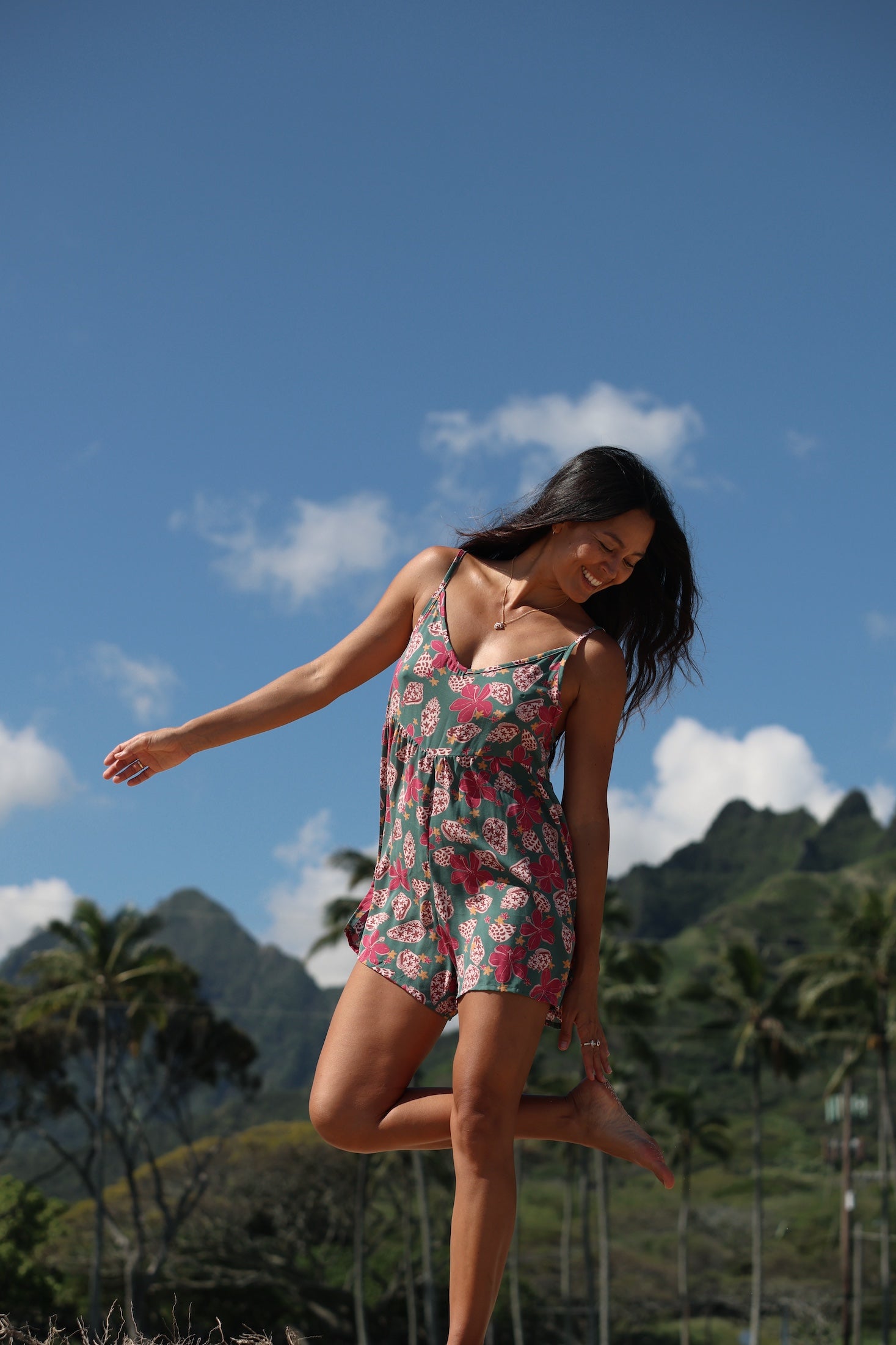 woman with brown hair wearing a spghetti strap romper with shell and pua print in a teal color