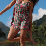 woman with brown hair wearing a spghetti strap romper with shell and pua print in a teal color