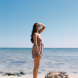 woman with brown hair wearing a spghetti strap romper with shell and pua print in a teal color