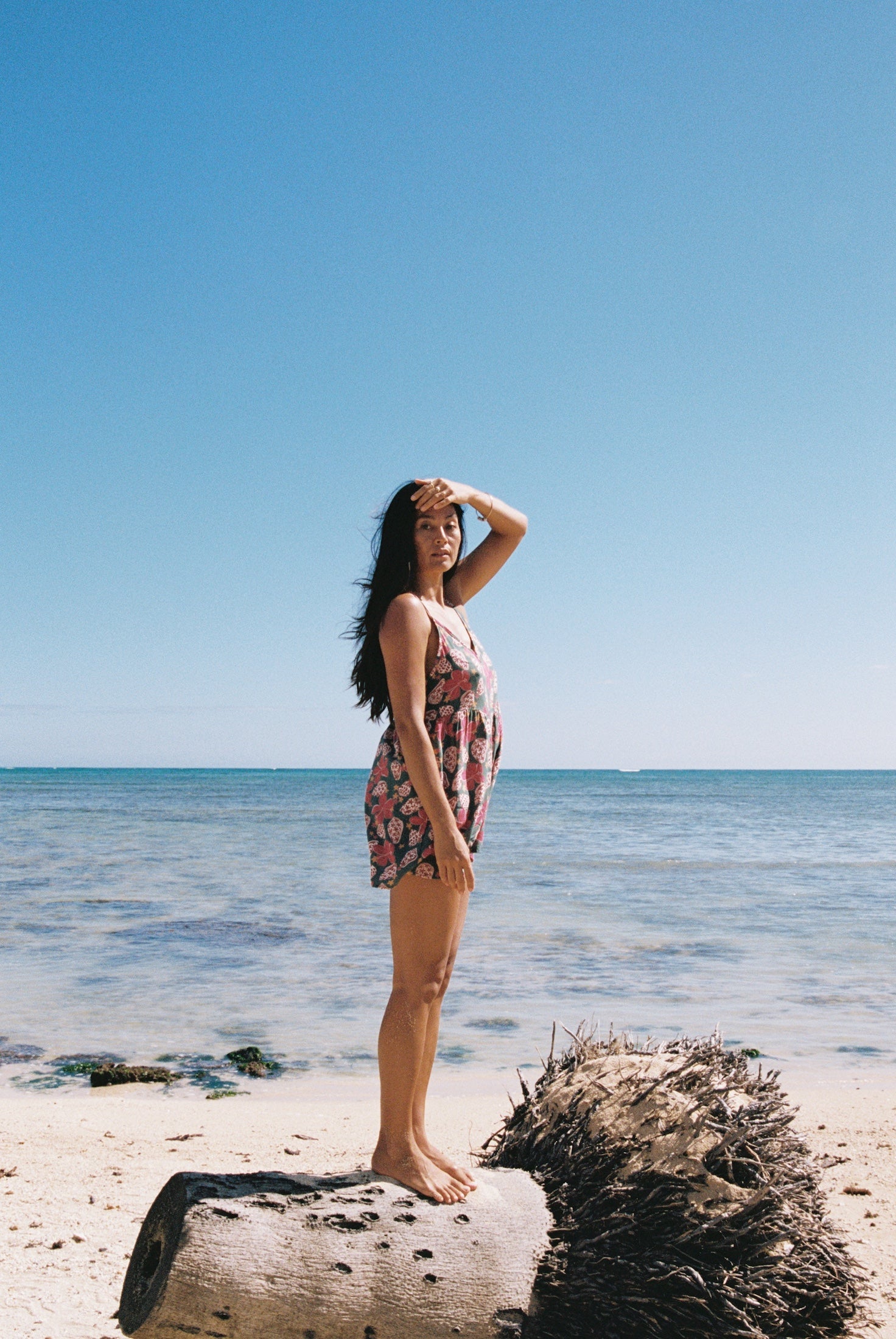 woman with brown hair wearing a spghetti strap romper with shell and pua print in a teal color