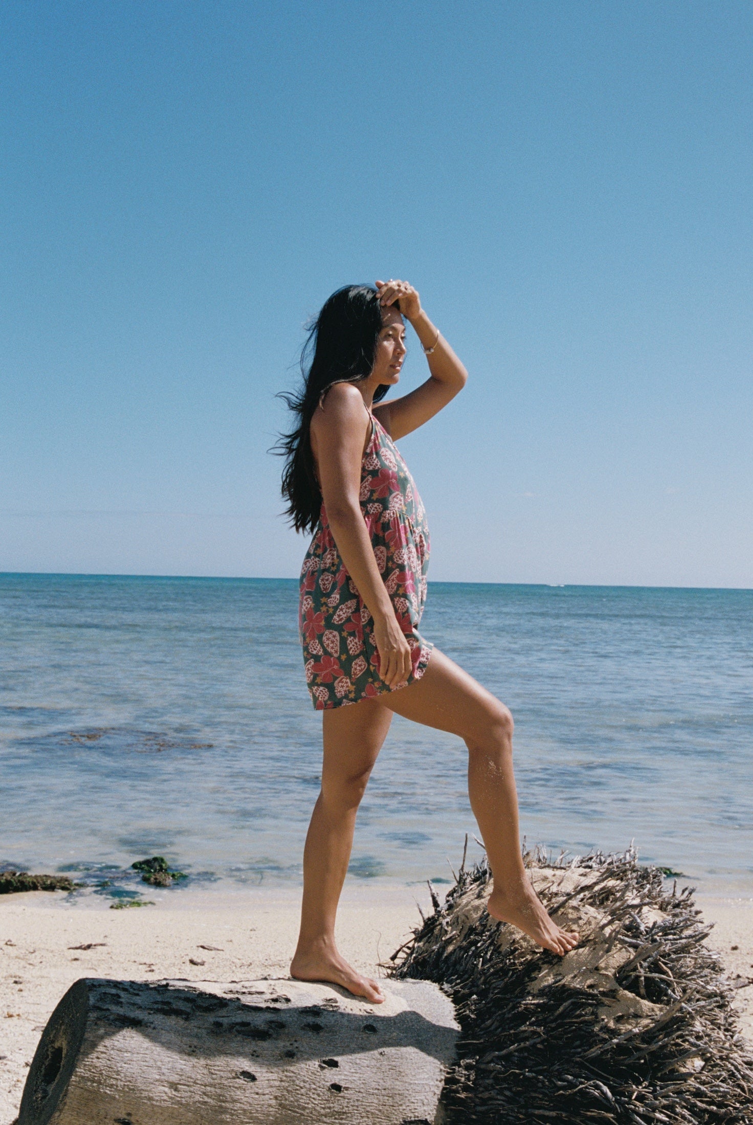 woman with brown hair wearing a spghetti strap romper with shell and pua print in a teal color