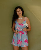 Woman in short sleeveless romper with pink floral print on light blue ground.