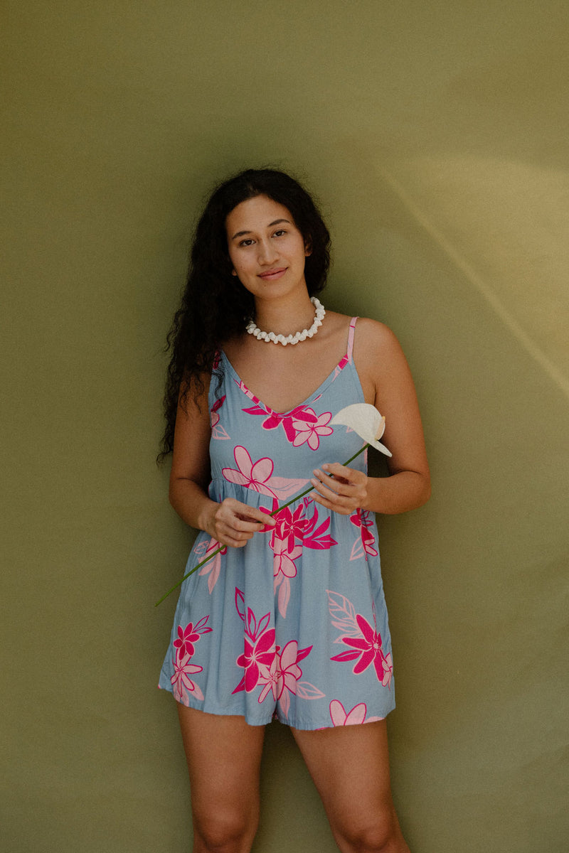 Woman in short sleeveless romper with pink floral print on light blue ground.