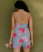 Woman in short sleeveless romper with pink floral print on light blue ground.