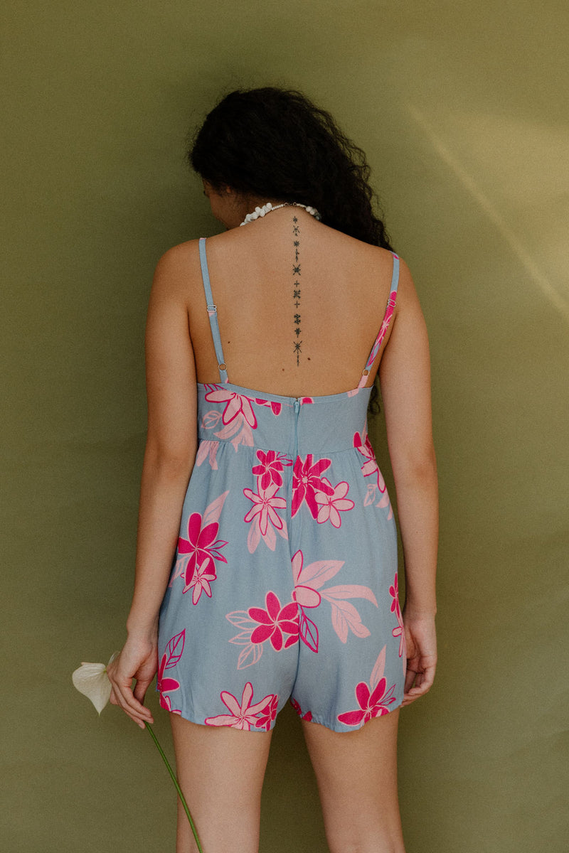 Woman in short sleeveless romper with pink floral print on light blue ground.