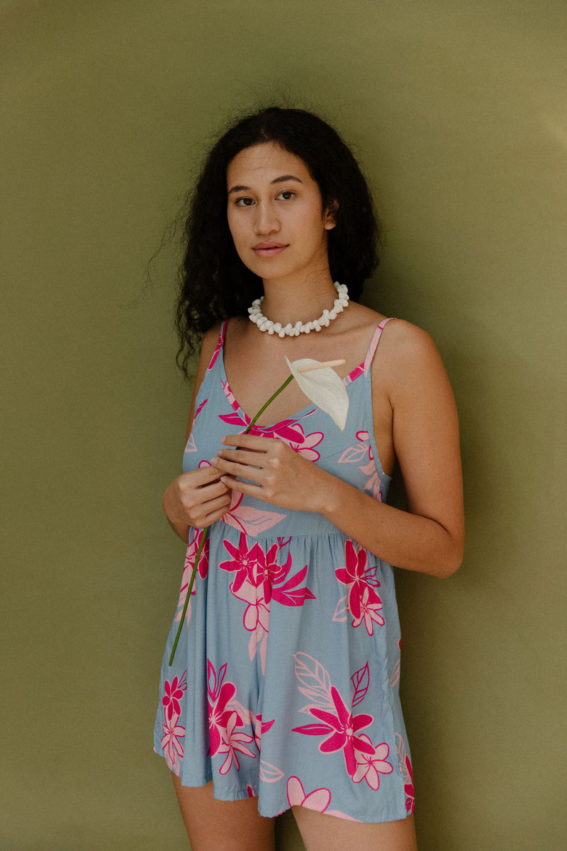 Woman in short sleeveless romper with pink floral print on light blue ground.