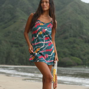 woman with dark brown hair wearing mini spaghetti strap dress in dark teal with shell and lei print